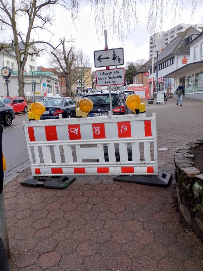 Verkehrsschild in der Bahnhofstraße Reinbek mit der Anweisung Fußgänger bitte andere Straßenseite benutzen aufgrund der Sparkassen-Baustelle.